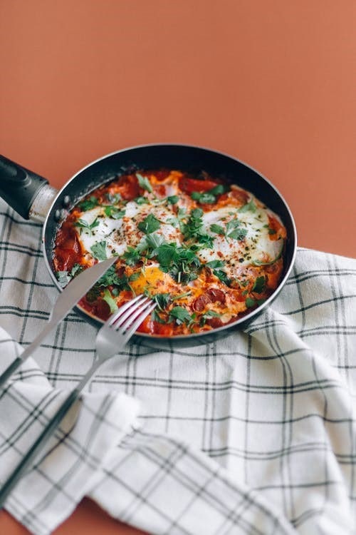 A skillet of shakshouka with a knife and fork-min